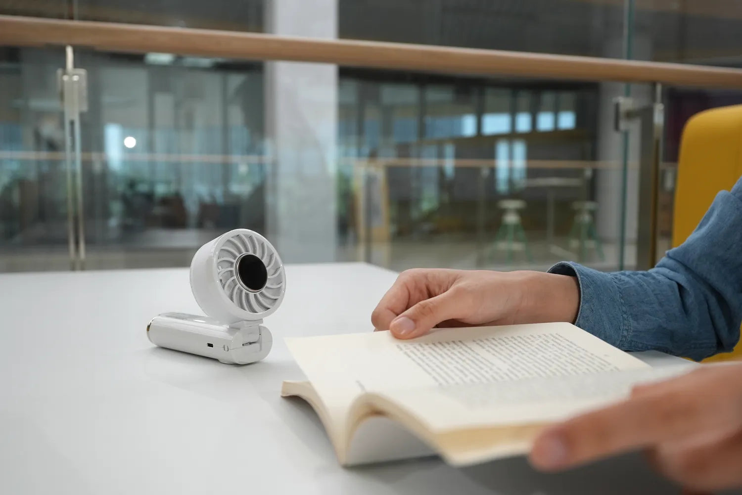 Airdog F200 handheld cooling fan folded into desk-stand mode beside someone reading