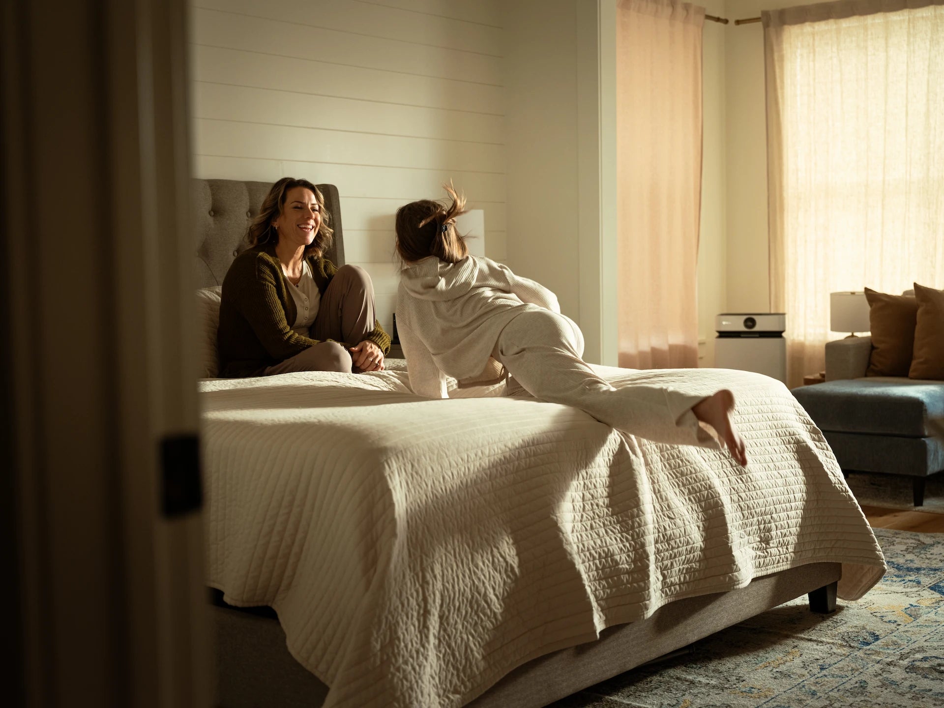 Two people on a bed in a sunlit bedroom, AirSoap X8 in the background